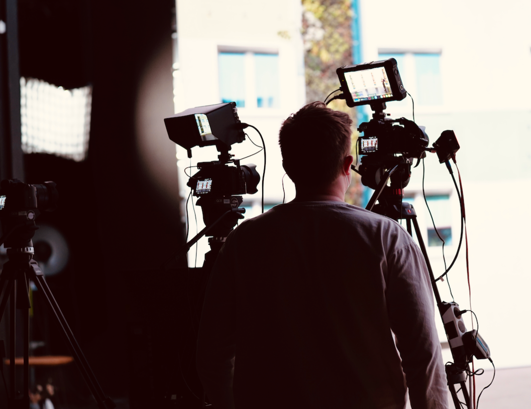 Ein Mann steht vor einer Kamera auf einem Stativ.