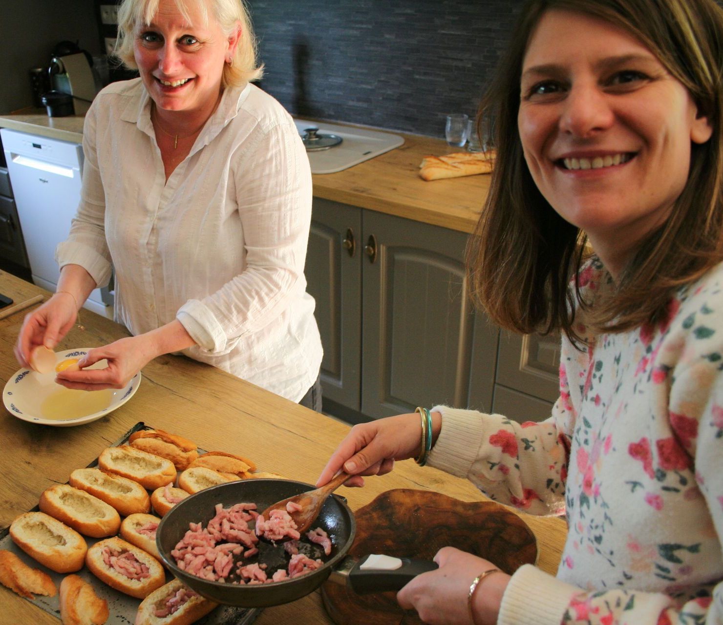 Two women are preparing food in a kitchen and smiling