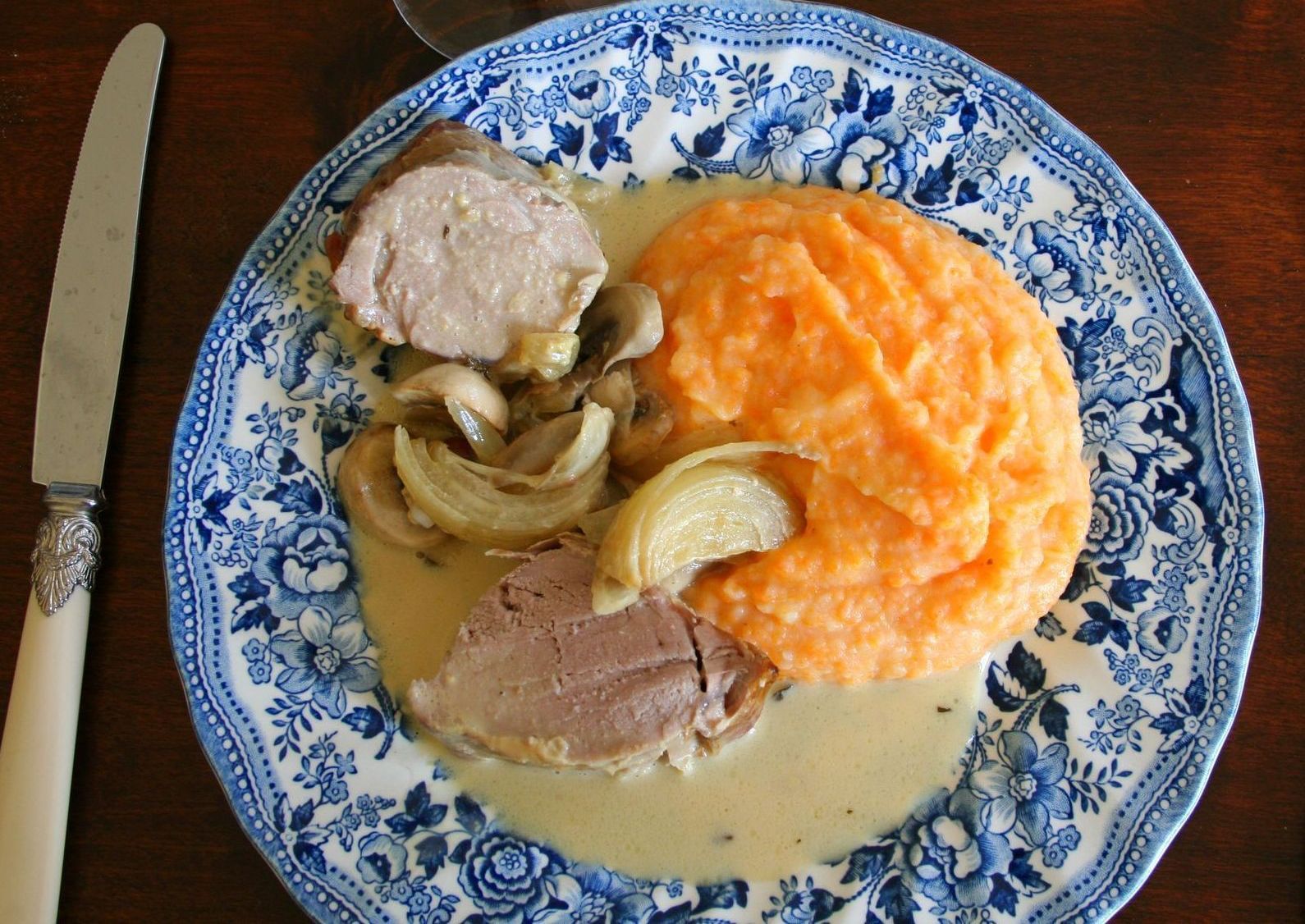 A blue and white plate topped with meat and mashed potatoes
