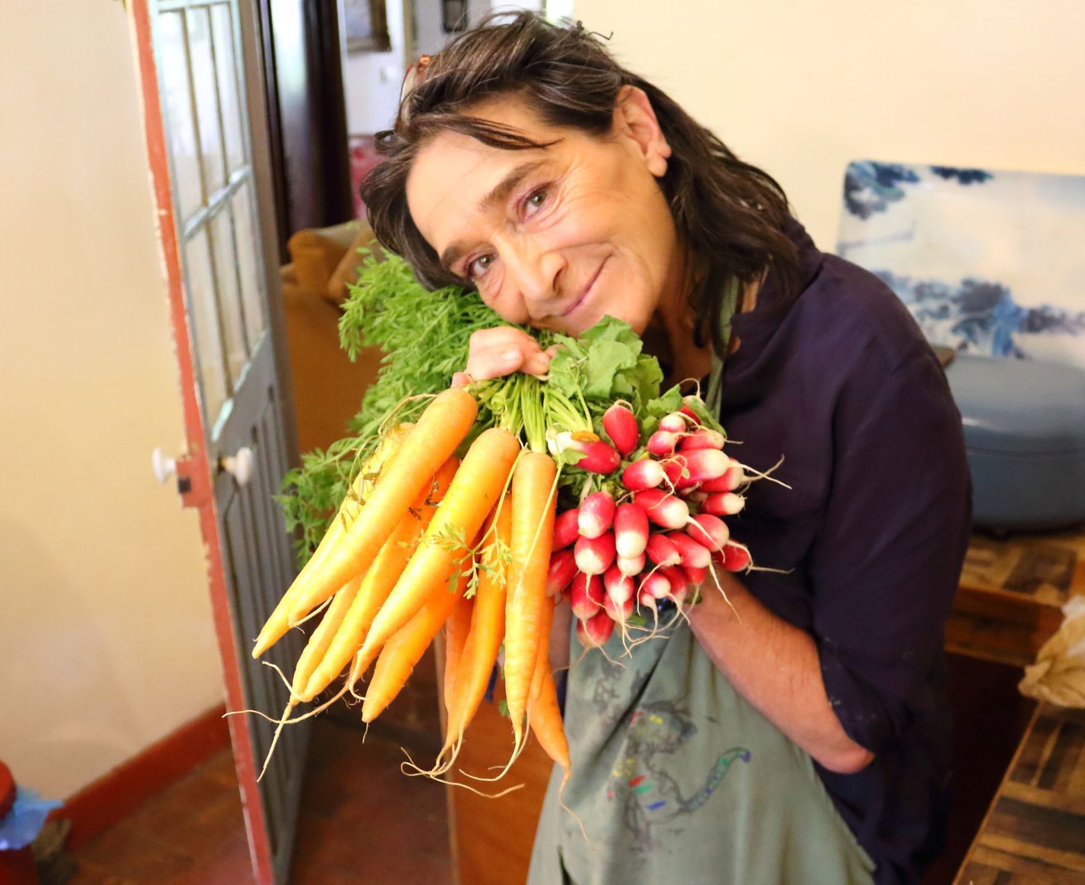 A woman is holding a bunch of carrots and radishes