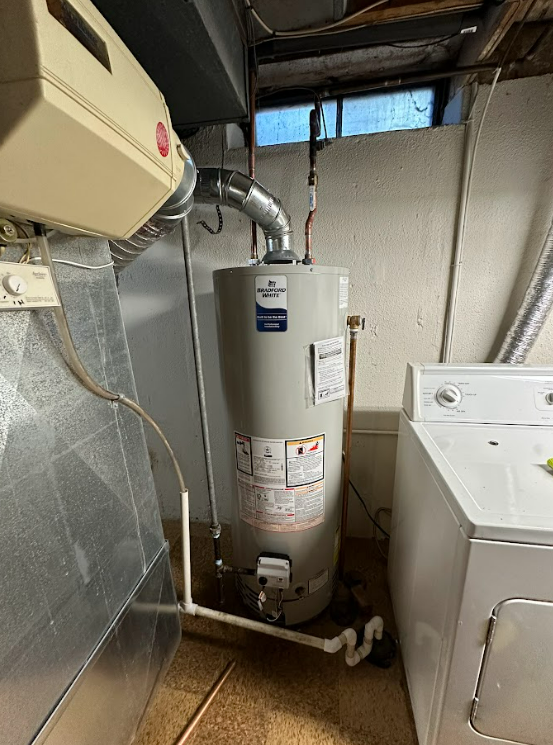 A water heater is sitting next to a washer and dryer in a laundry room.