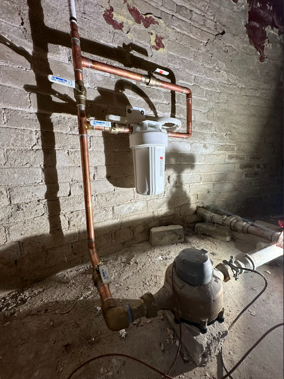 A water meter is attached to a copper pipe in a basement.