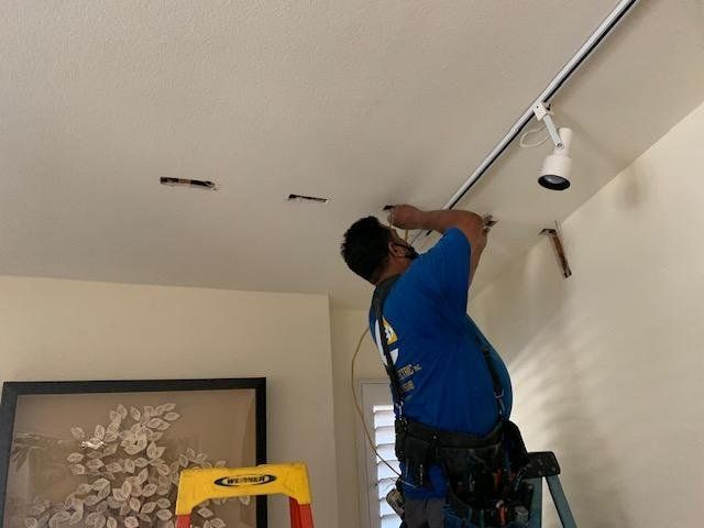 A man is standing on a ladder fixing a light on the ceiling.