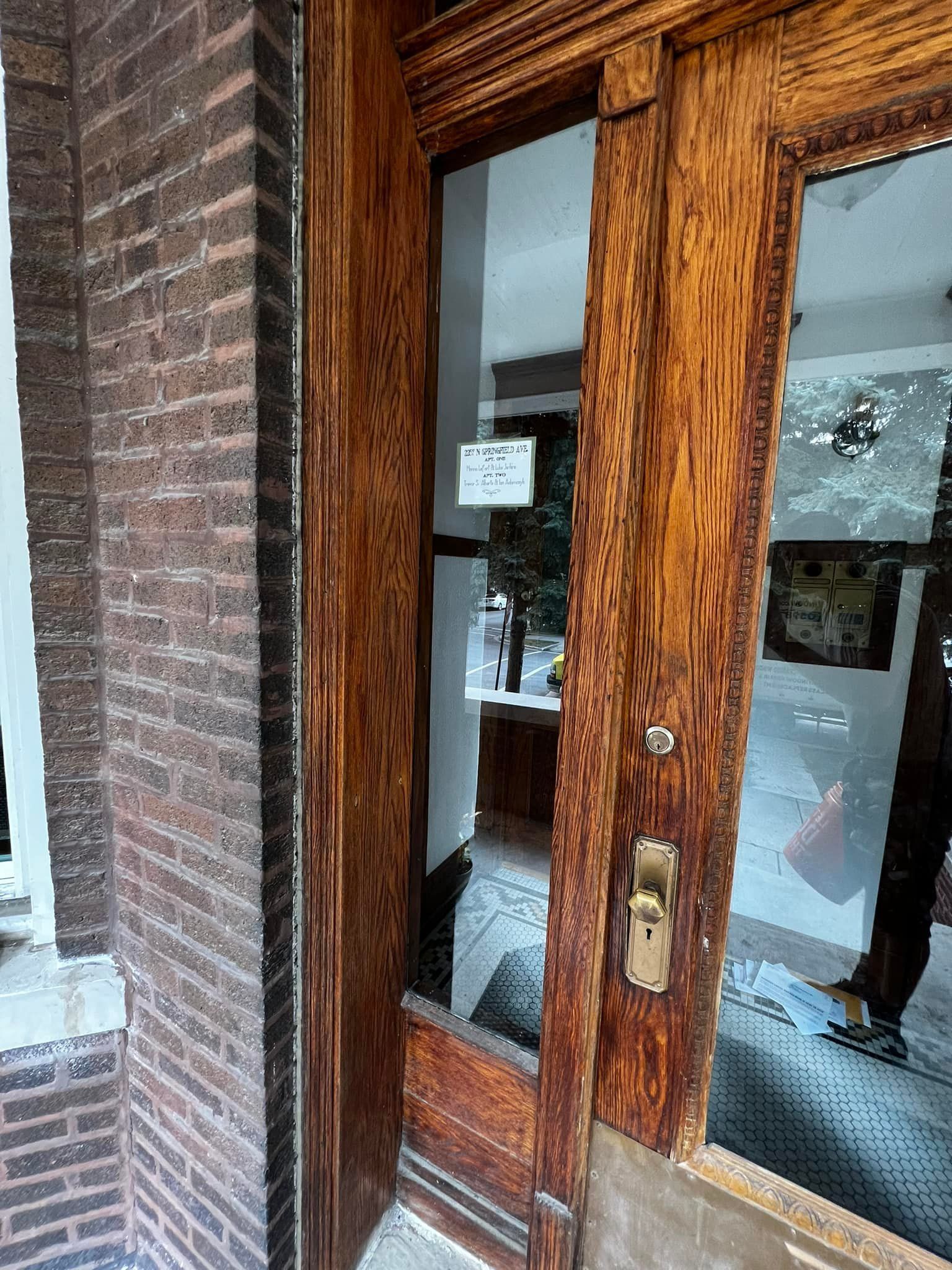 A wooden door with a glass window is next to a brick wall.