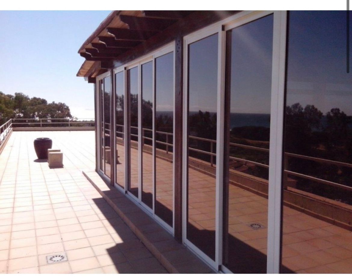 Glass doors on a patio reflect the sky and surrounding landscape. White frames. Brown roof overhang.