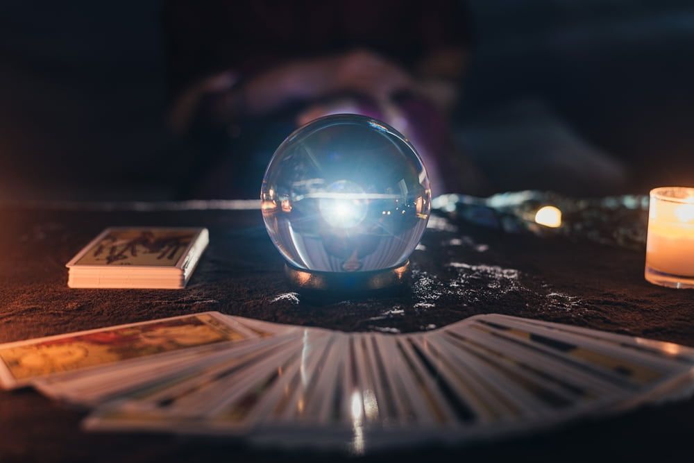 Crystal ball on table with tarot cards and candles.