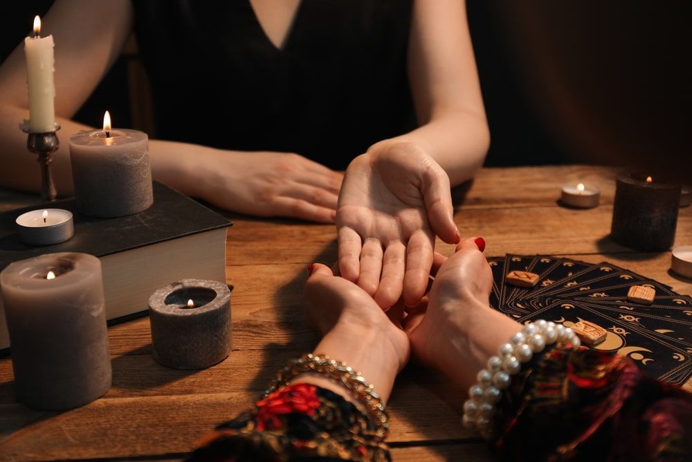Hands open for palm reading with candles on a wooden table.