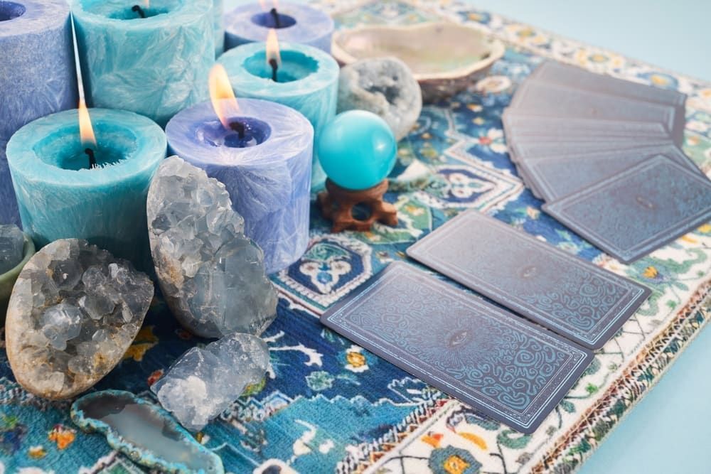 Blue candles, tarot cards, crystals, and a crystal ball on a patterned cloth.