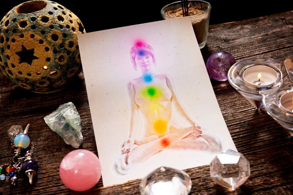 Drawing of person with chakra colors, surrounded by crystals, candles, and a lantern on a wooden table.