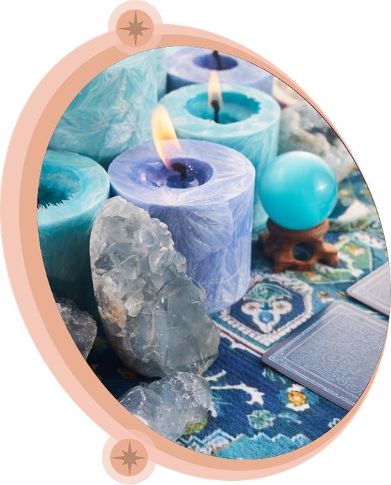 Blue candles, crystals, a crystal ball, and tarot cards on a blue patterned cloth.