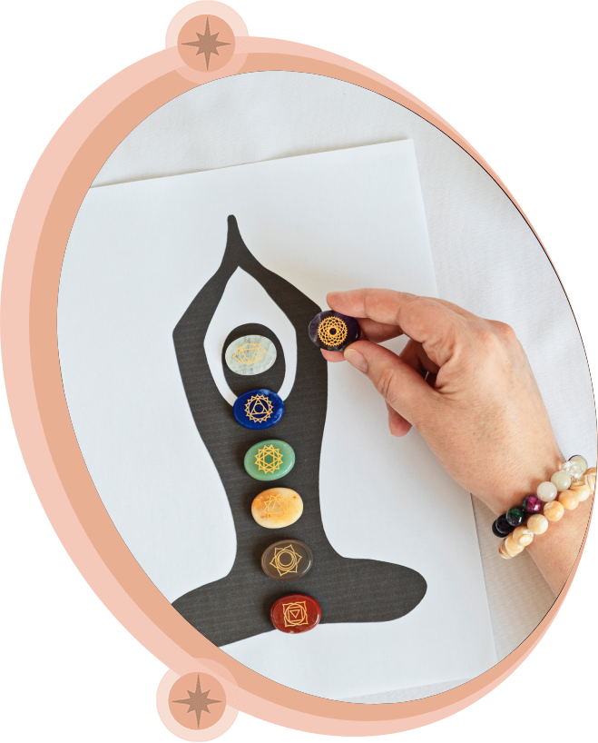 Hand placing chakra stone on a drawing of a person in a yoga pose; stones aligned with chakras.