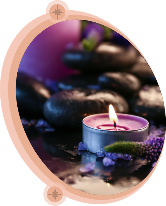 Candle lit next to a stack of black rocks with purple flowers.