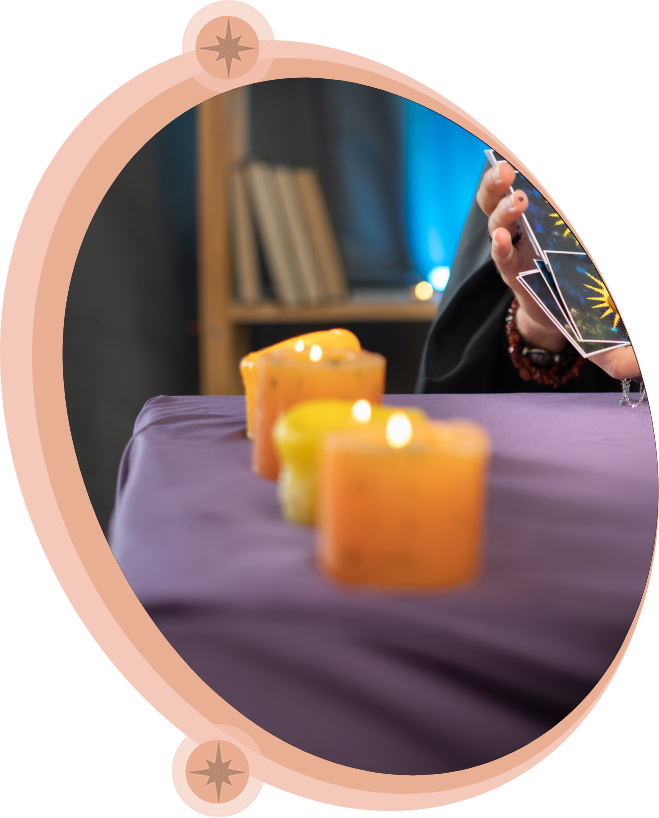Person holding tarot cards, candles on a purple table, interior setting.