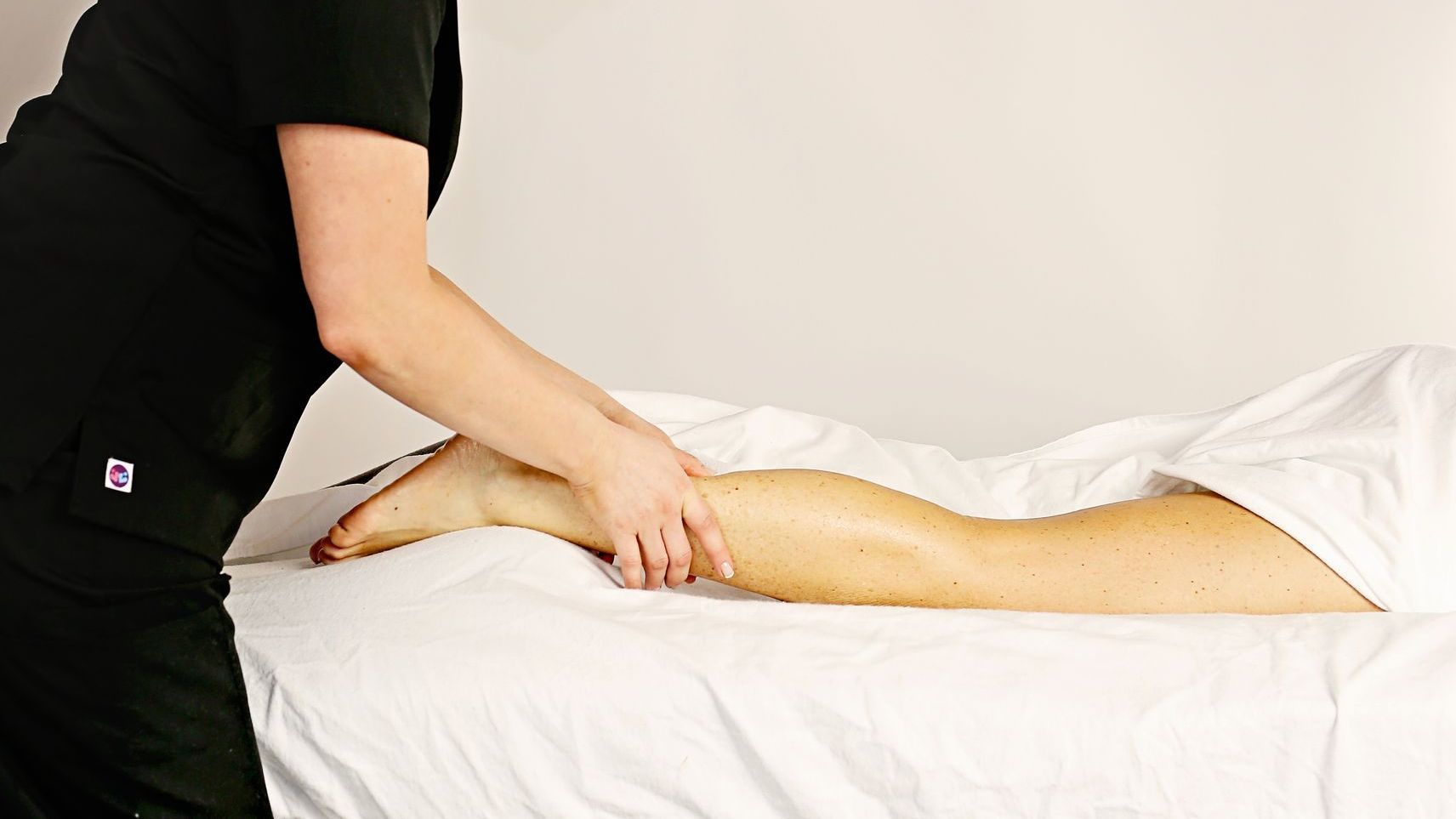 A woman is giving a leg massage to a person laying on a bed.