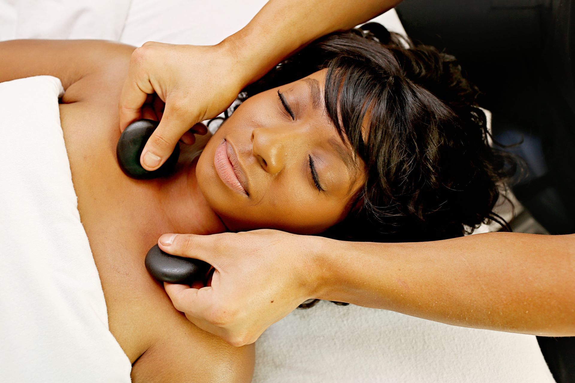a woman with her eyes closed is getting a massage with hot stones at A Touch of Recovery in Plymouth, MI