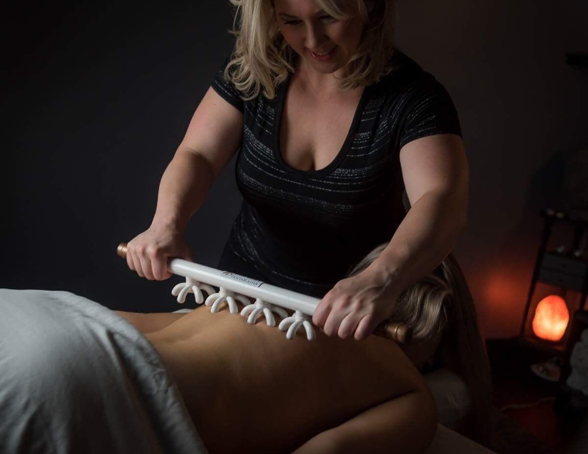 Sarah, owner of A Touch of Recovery, is giving a massage to a woman with a fascia blasting tool