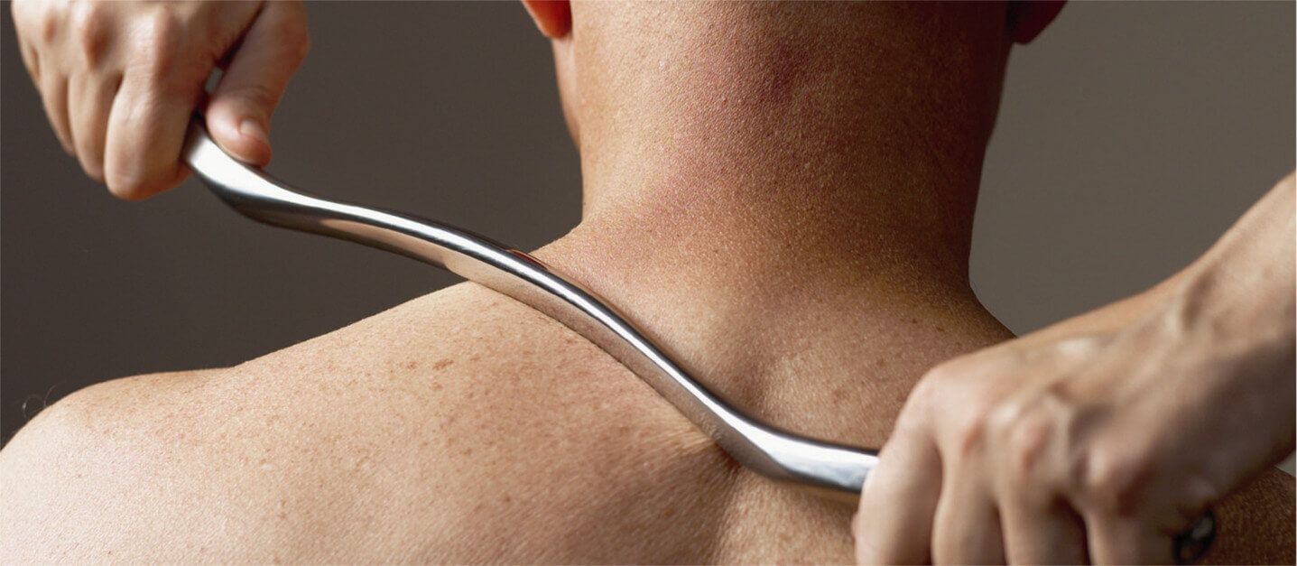 A man is getting a massage with a metal tool on his neck.