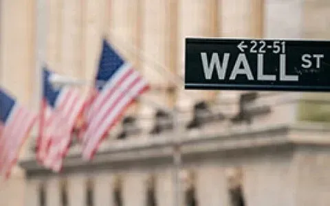 Wall Street street sign with American flags and building facade in background.