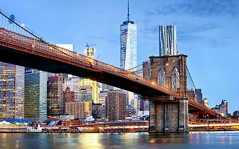Brooklyn Bridge spans over water with NYC skyline in background.