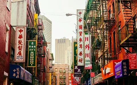A narrow street in Chinatown, New York, lined with buildings and colorful signs in Chinese.