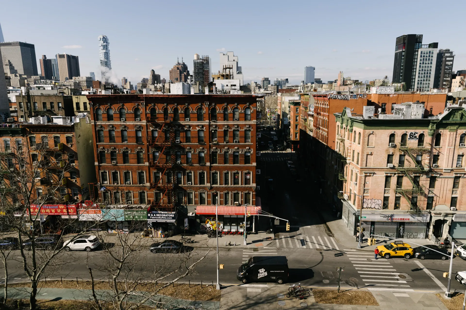 Buildings in NYC, a busy street below. Red brick building in the center. Clear sky.
