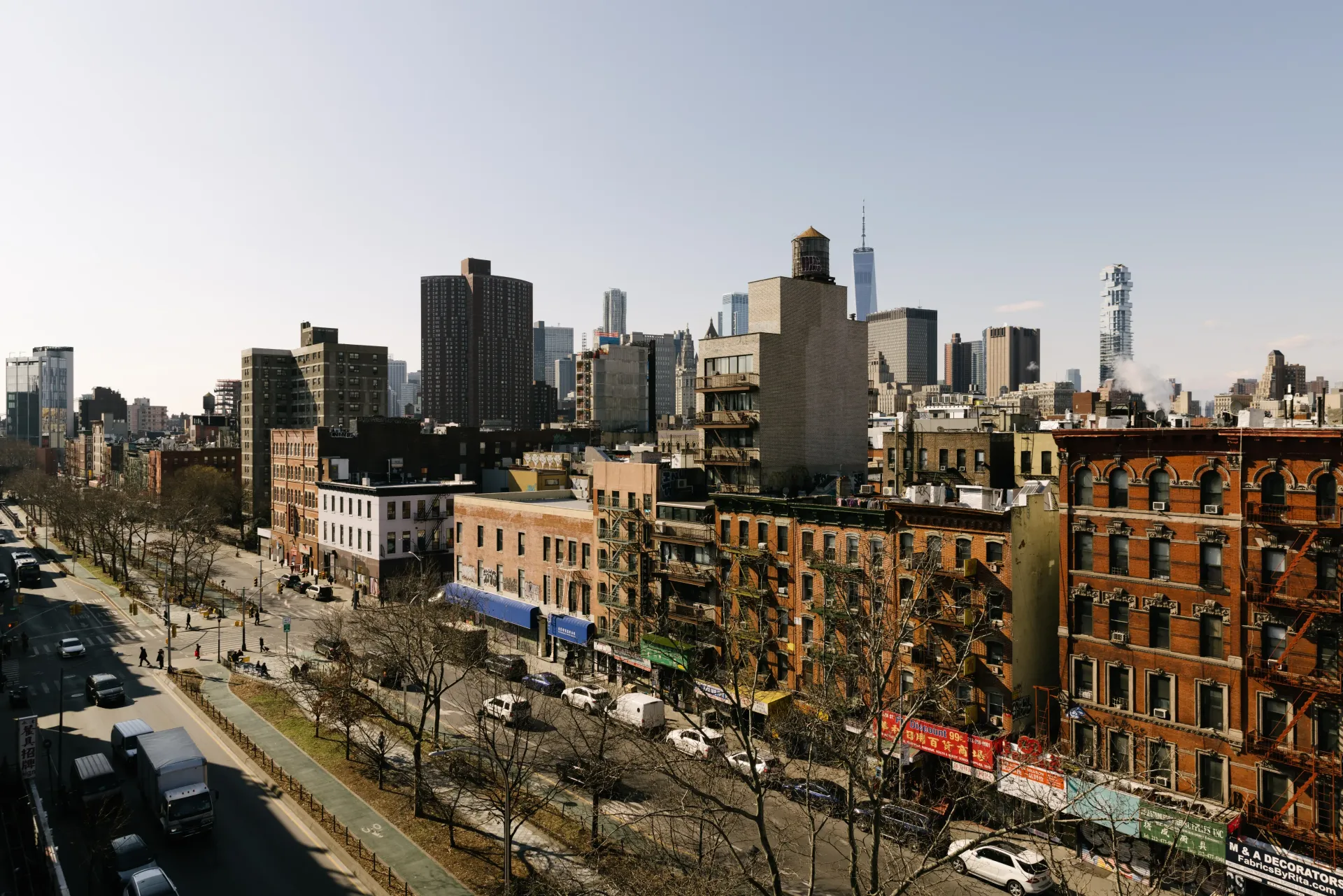 Cityscape view of buildings along a street, cars and trees below a clear sky.