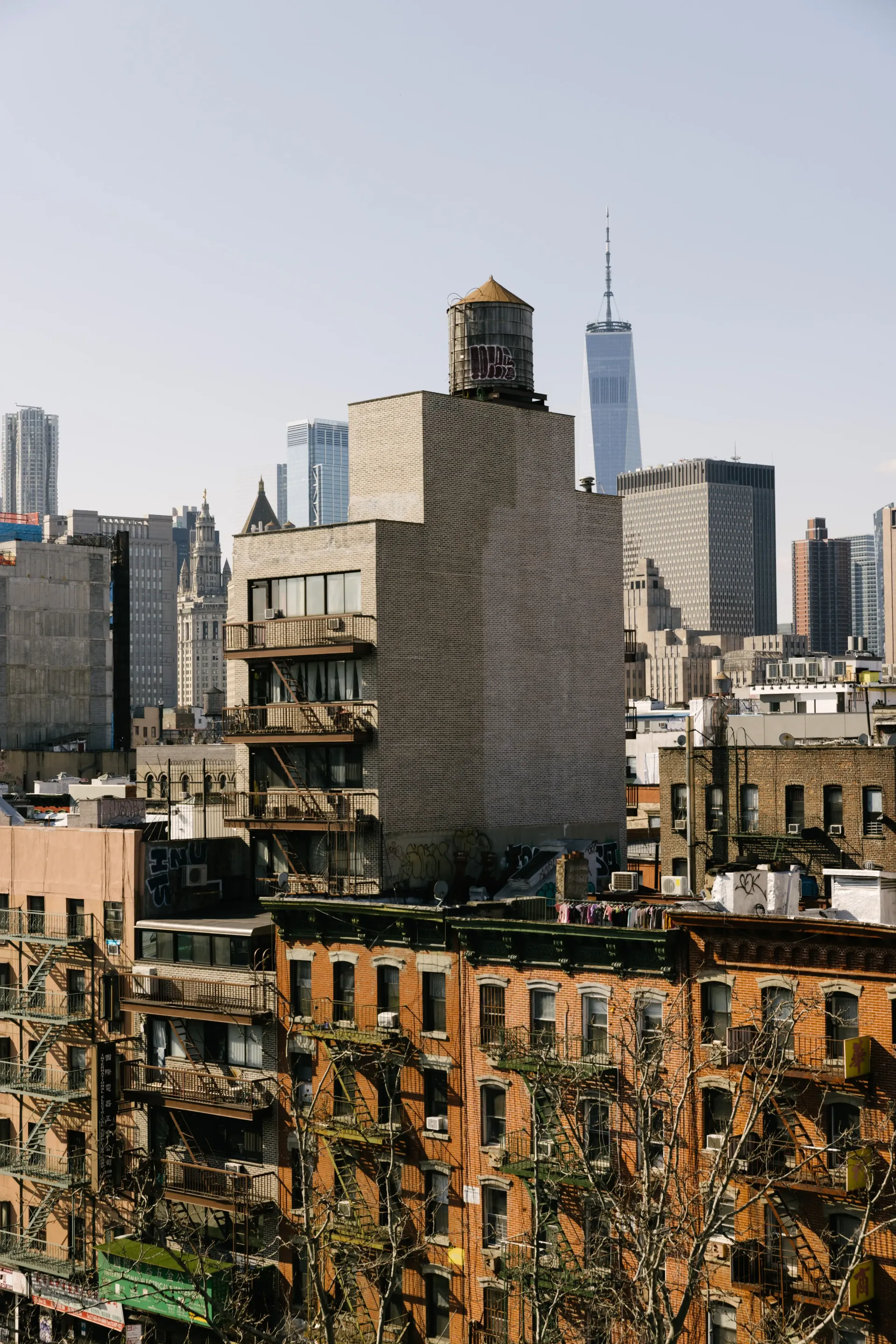 Cityscape with brick buildings and a water tower, the One World Trade Center is visible in the background.