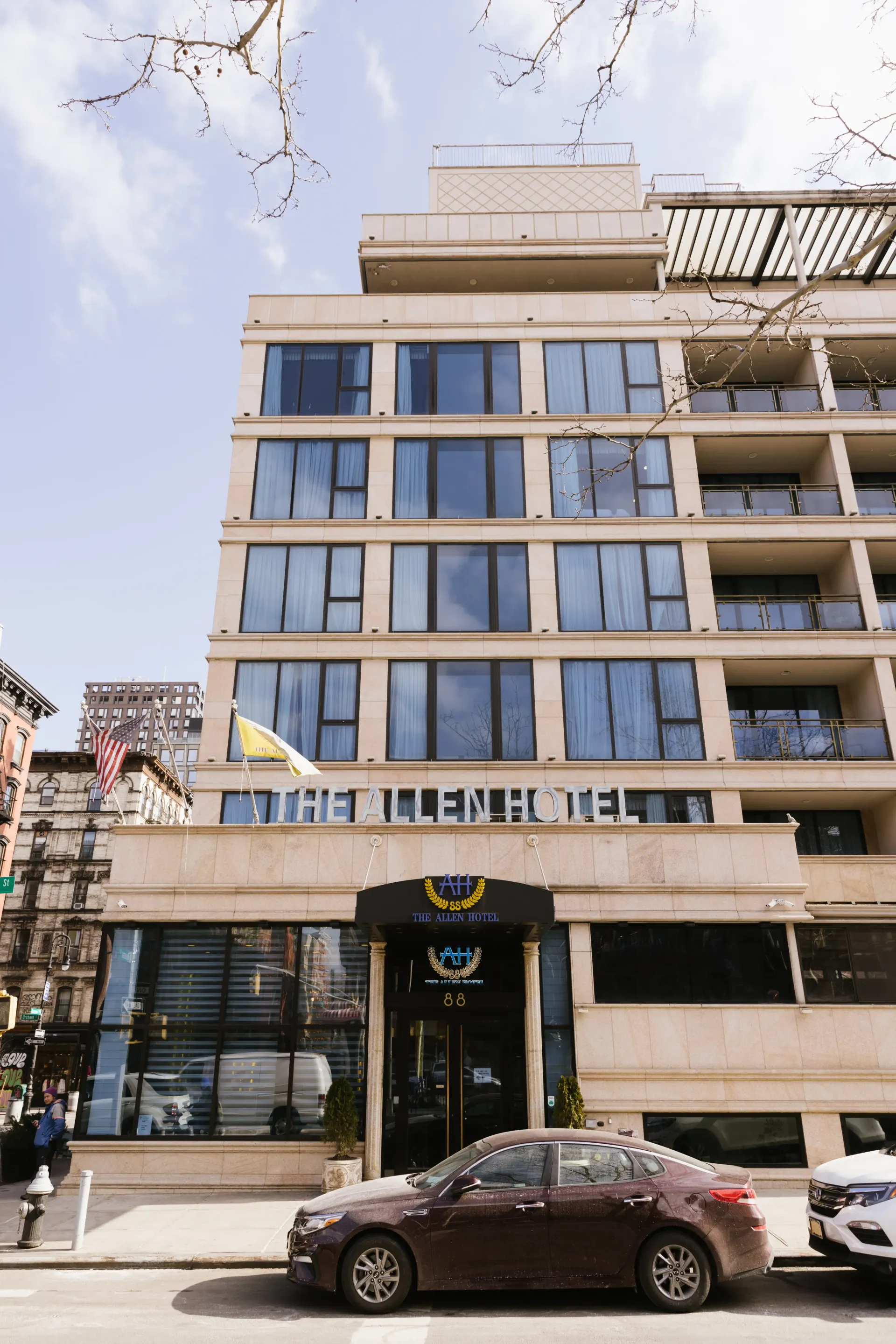 Hotel exterior on a sunny day with a brown car parked in front.