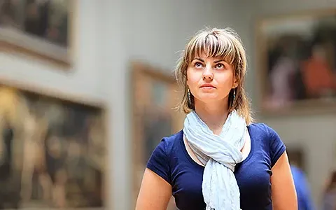 Woman in a museum looking at art, wearing a blue shirt and white scarf.