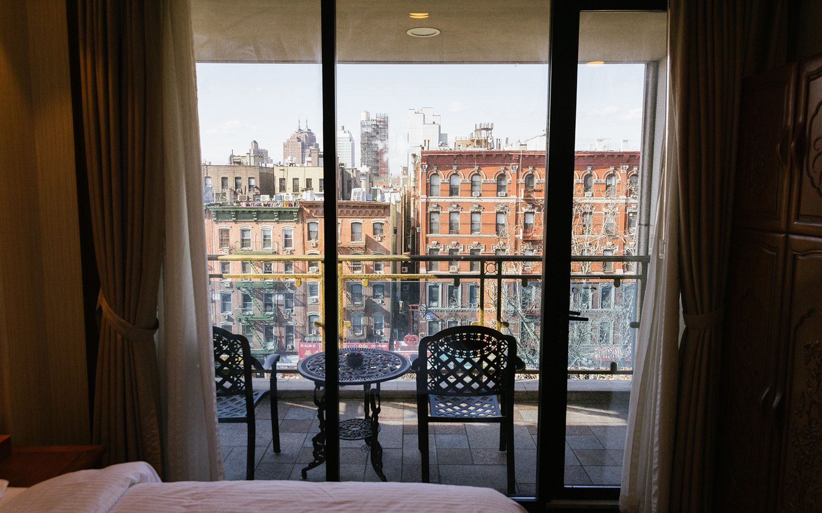 Balcony view of city buildings with table, chairs, and sheer curtains.