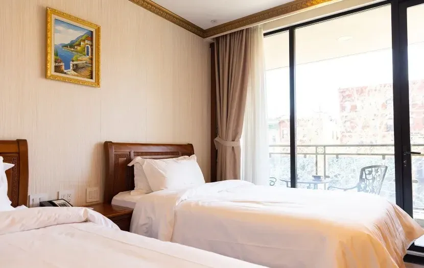 Two beds in a hotel room, with a balcony view and a painting on the wall.