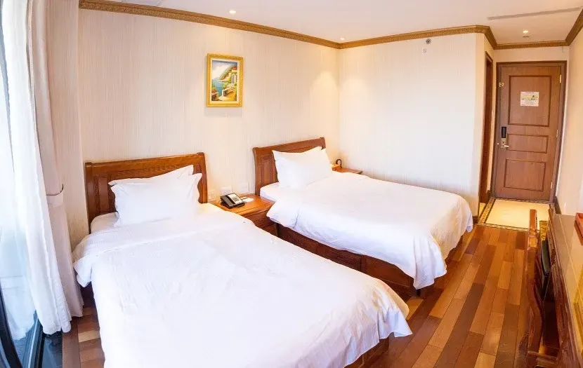 Two twin beds in a hotel room with light wood floors, white linens, and a closed door.