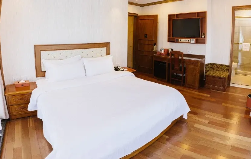 Hotel room with a bed, desk, TV, and wooden floor.