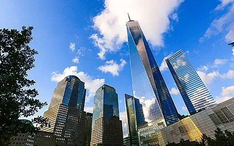Skyscrapers against a blue sky with fluffy clouds; One World Trade Center is prominent.