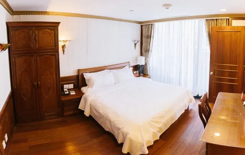 Bedroom with wooden furniture, including a bed, wardrobe, and desk, with white bedding and curtains.