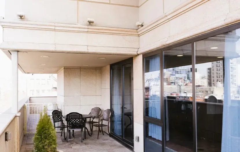 Balcony with table, chairs, glass doors, and city view.