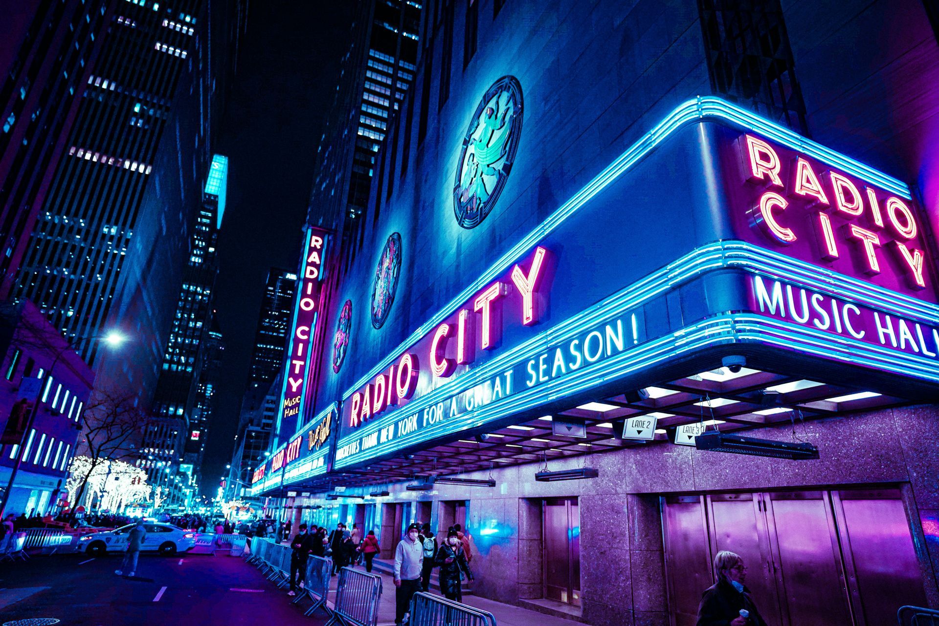 Radio City Music Hall at night, neon sign lit up. People enter building, street below.