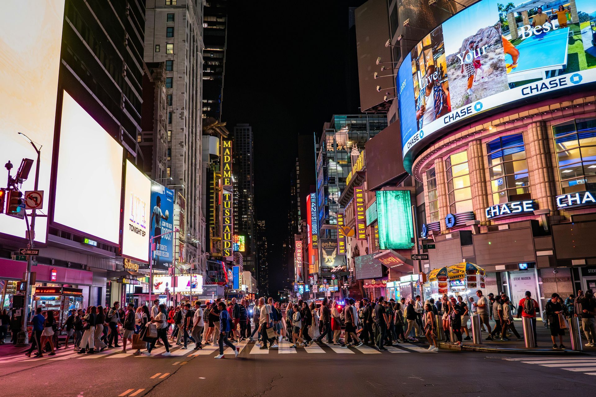 Times Square at night, crowds crossing street, bright billboards, skyscrapers.