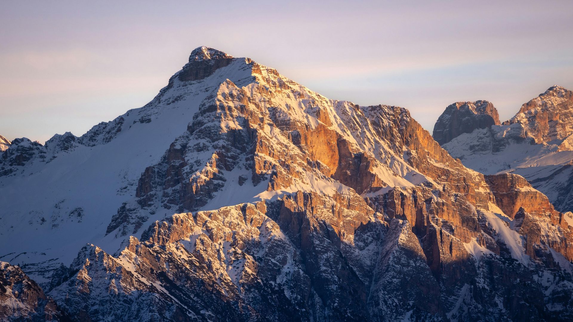Snow-covered mountain peaks lit by warm sunrise against a clear sky