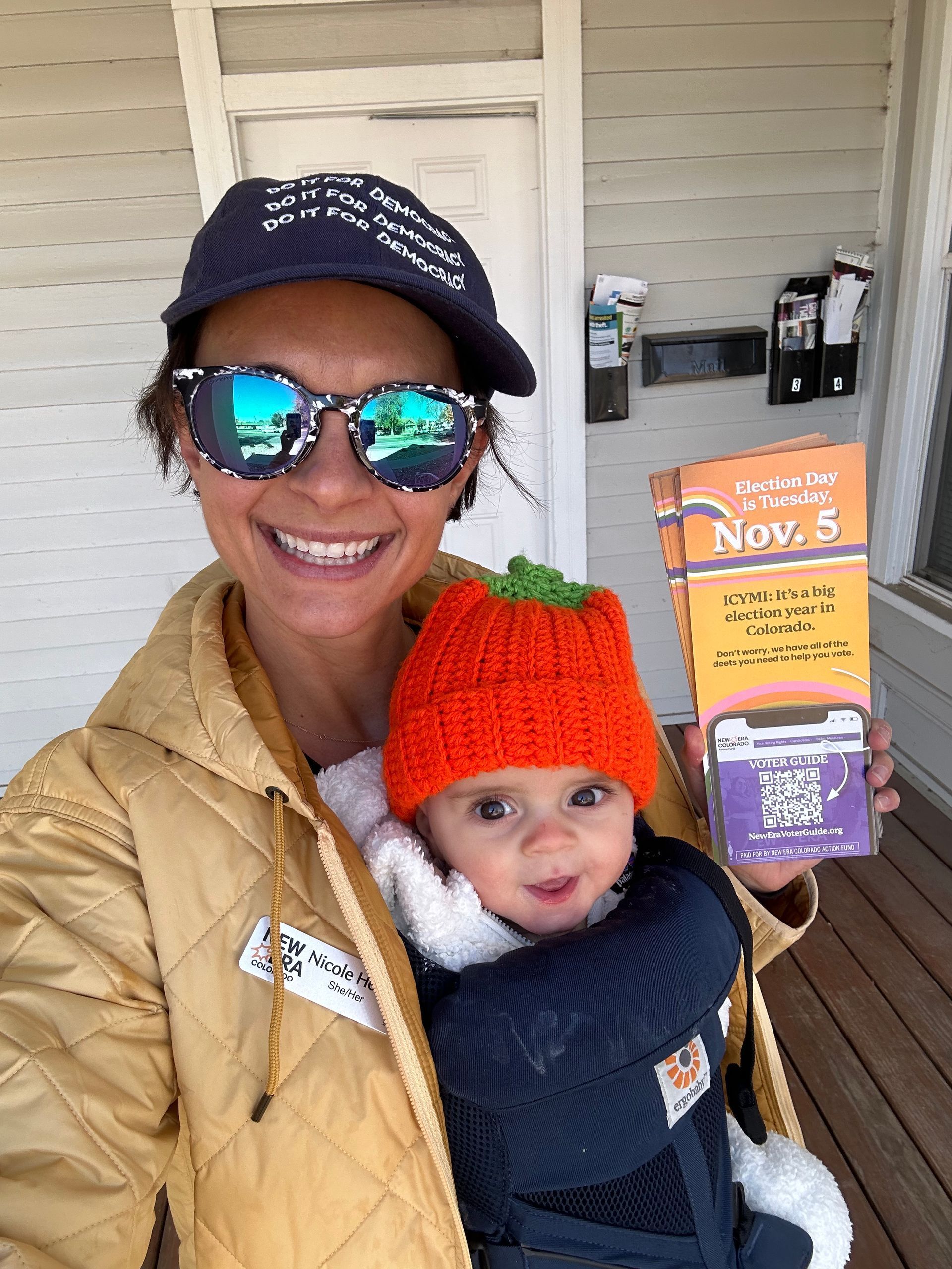 A woman is holding a baby wearing a pumpkin hat and sunglasses.