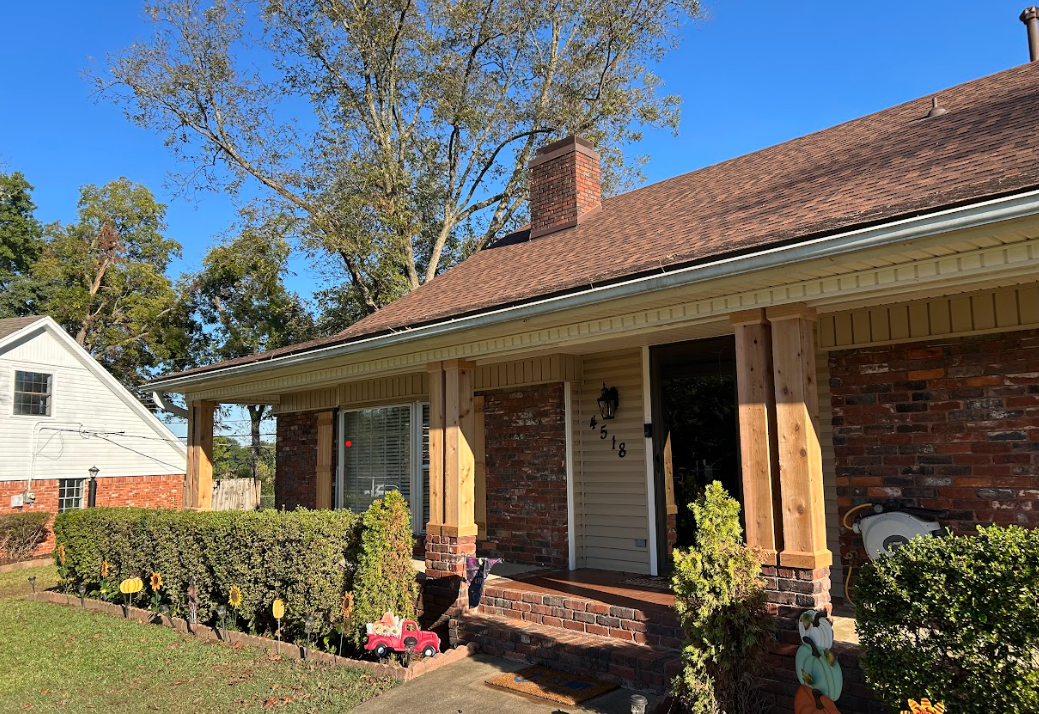 A brick house with a porch and a chimney on the roof.