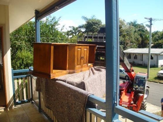 A Wooden Cabinet Is Being Lifted by A Tractor on A Balcony — Armstrong Removals in Ninderry, QLD