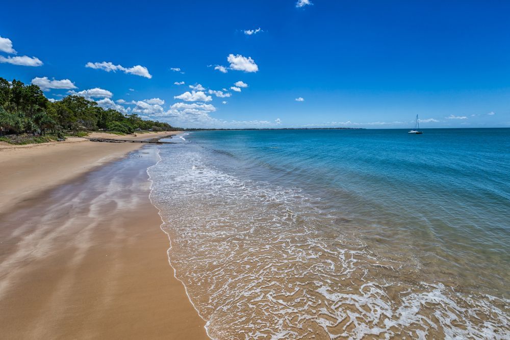 A Beach With Waves Crashing On The Sand And A Boat In The Distance  — Armstrong Removals in Hervey Bay, QLD