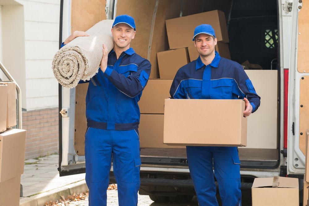 Two Men Are Carrying Boxes And A Rug In Front Of A Moving Van — Armstrong Removals in Mackay, QLD