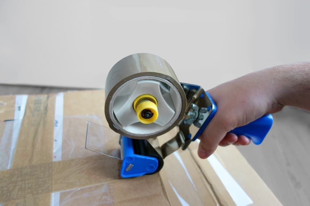A Person Is Holding a Tape Dispenser Over a Cardboard Box — Armstrong Removals in Ninderry, QLD