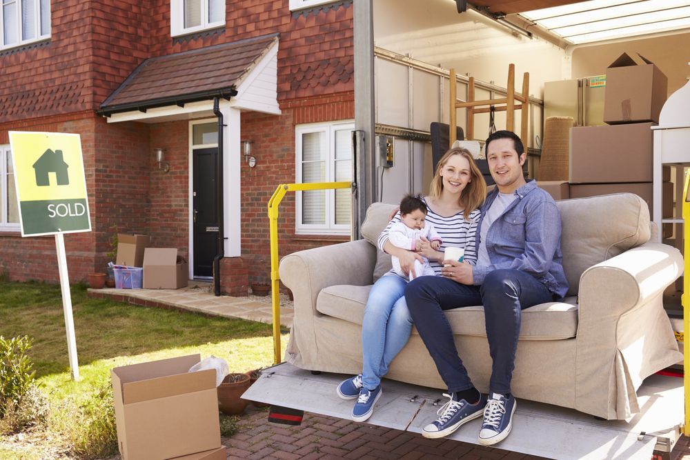 A Family Is Sitting On A Couch In Front Of A House — Armstrong Removals in Townsville, QLD