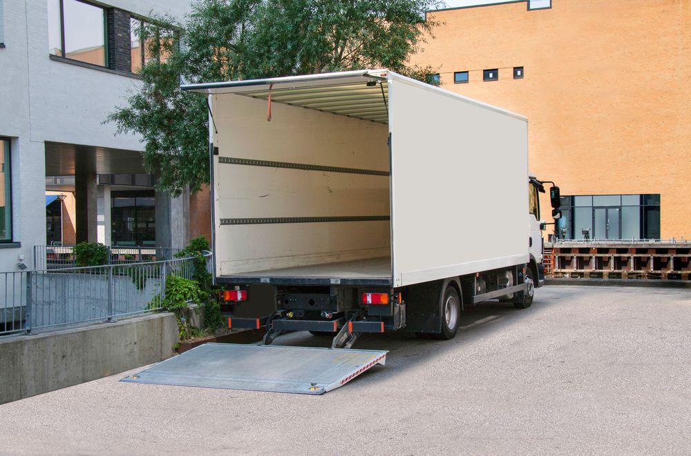 Delivery truck with lowered ramp at a loading dock near buildings.