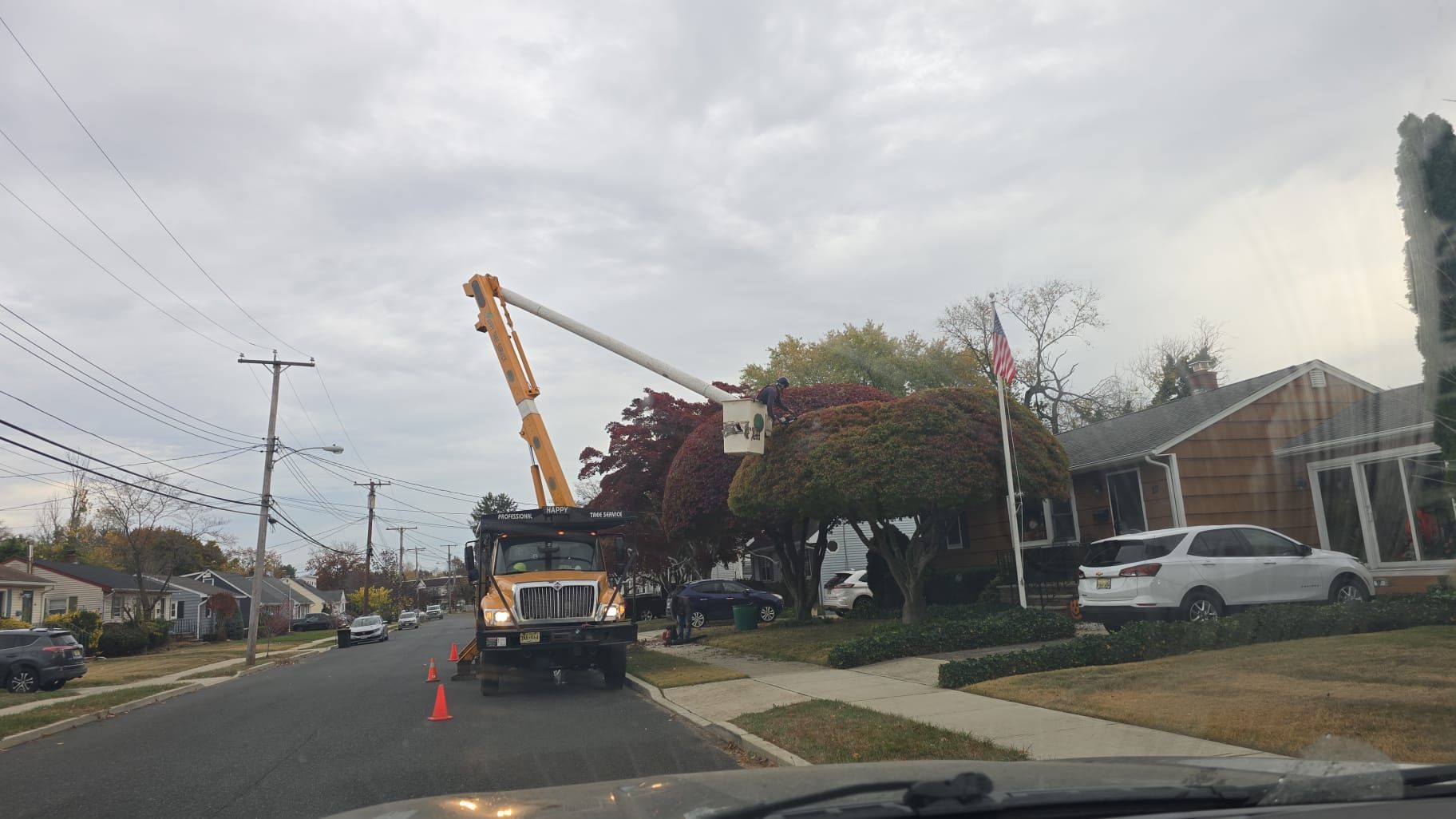 A truck with a crane on top of it is cutting trees in a residential neighborhood.
