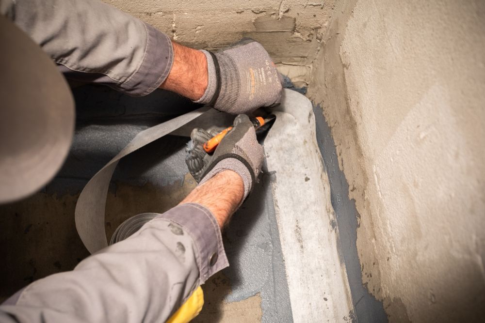 A Man is Cutting a Piece of Tape With a Pair of Scissors — Legend Waterproofing In North Sydney, NSW
