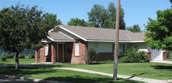 A brick and white ranch-style house on a green lawn, sidewalk in front, blue sky.